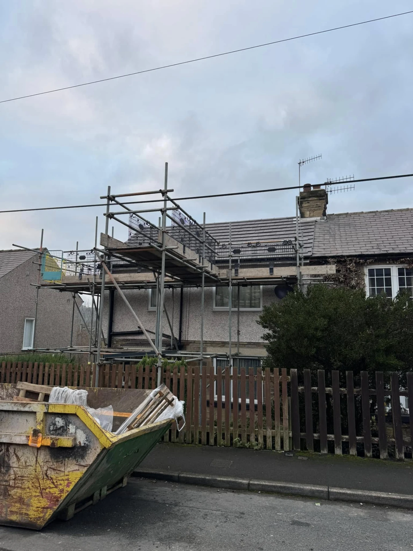 Street-level view of a house with scaffolding and a waste skip